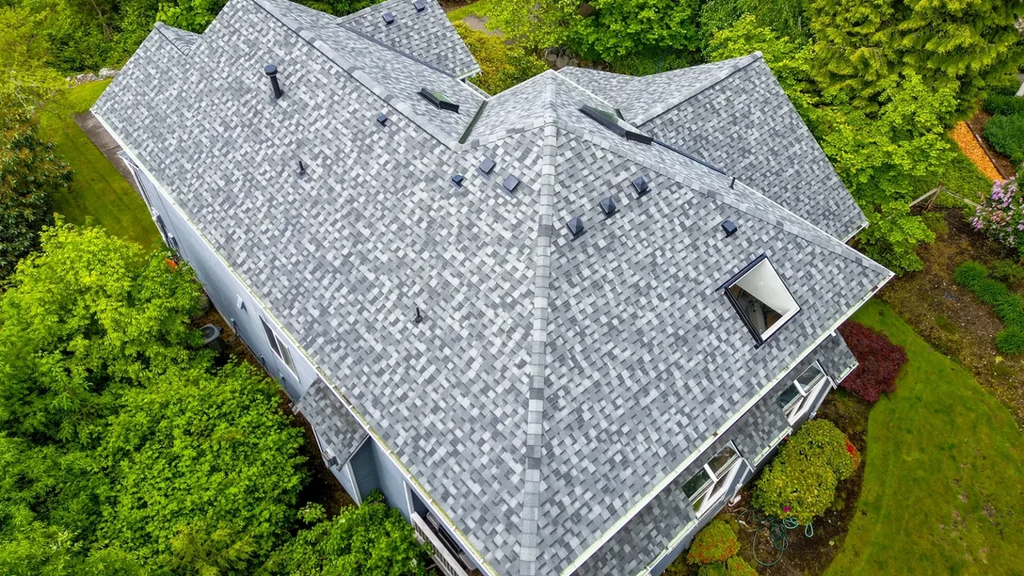 Aerial view of a new asphalt shingle roof on a home among tall trees, roof replacement