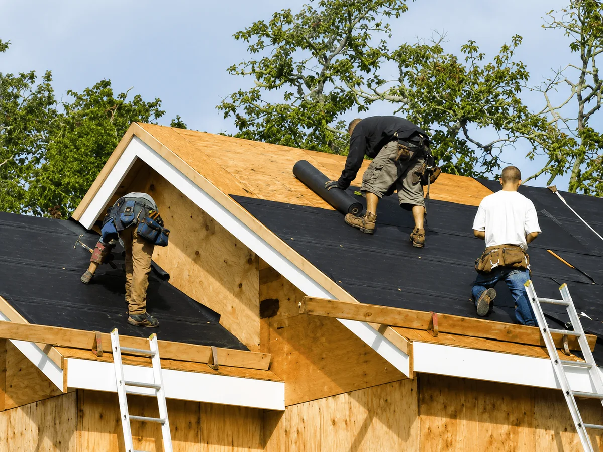 Three roofers laying underlayment on the new sheathing of a framed house, new construction roofing