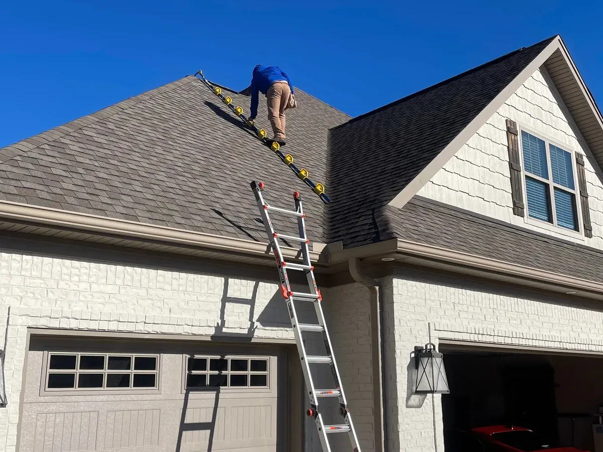 Roofer climbing a roof ladder up an asphalt shingle roof for roof inspections