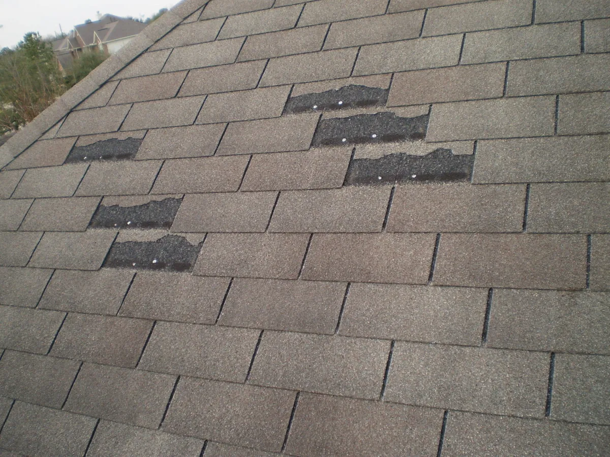 Asphalt shingle roof with several tabs blown off, damage that calls for roof repair