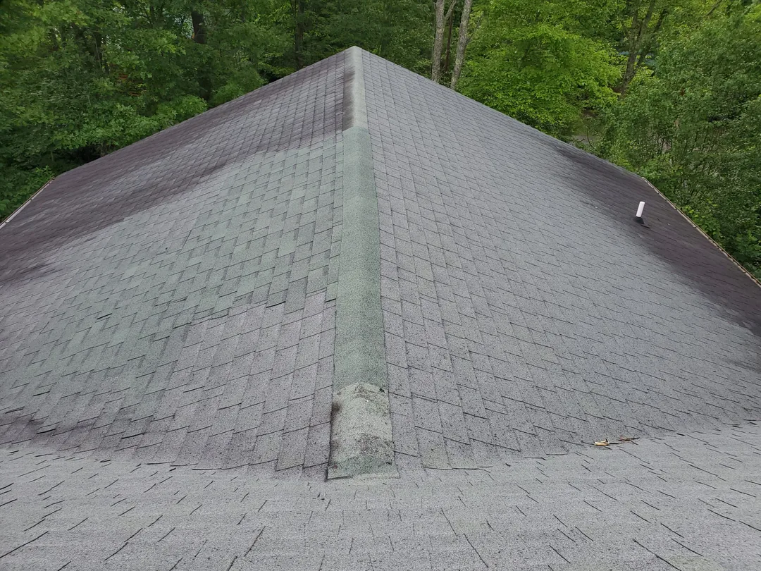 Worn shingle roof hip with a patched ridge cap from an earlier roof repair
