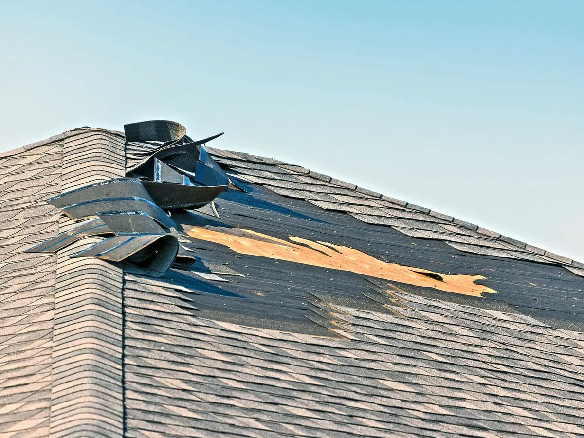 Wind torn asphalt shingles peeled back near a roof ridge, damage that calls for roof repair